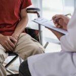 Male patient sitting and consulting a doctor with his hand holding his crotch