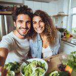 Selfie picture of young happy couple preparing healthy salad meal in their kitchen at home